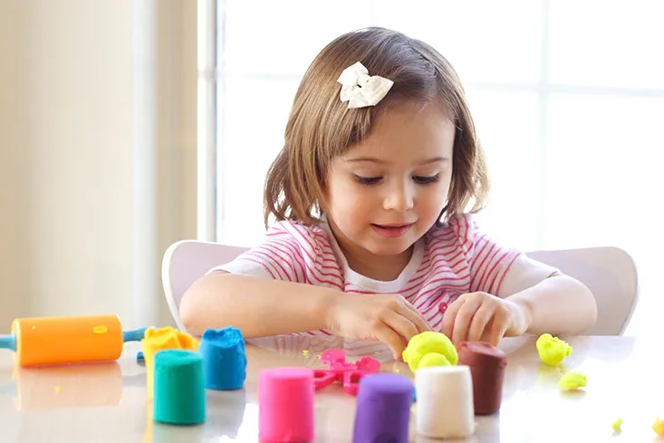 A little girl playing with play dough on the table.