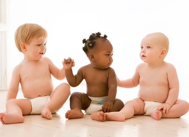 Three babies sitting on the ground holding hands.
