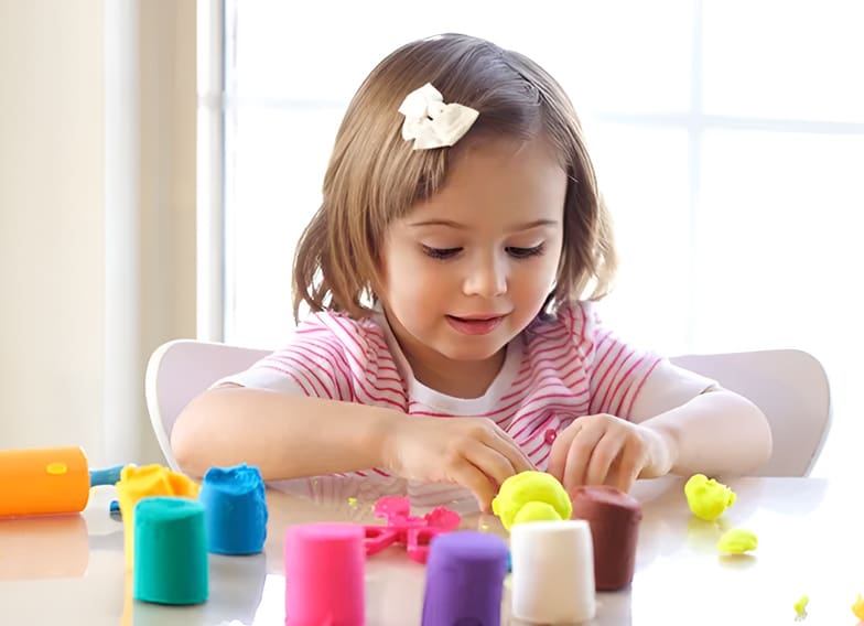 A little girl playing with play dough at the table.